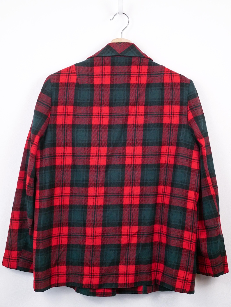 May include: A red, black, and green plaid blazer hanging on a silver hanger. The back of the blazer is visible, showcasing the classic pattern. The fabric appears to be a medium weight, suitable for cooler weather.