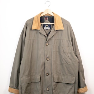 May include: An olive green jacket with a tan corduroy collar and matching corduroy sleeve cuffs. The jacket features a front button closure, two large lower flap pockets, one chest pocket, and a plaid interior lining. A Woodlake brand label is visible.