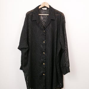 May include: A black long-sleeve button-down shirt made of a sheer, semi-transparent fabric featuring a subtle, wavy, tone-on-tone textured pattern. The shirt has a classic collar, cuffed sleeves, and small, diamond-shaped gold-toned buttons.