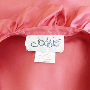 May include: A pink cotton blouse with a ruffled neckline and a white label that reads "JESSIE" with a trademark symbol.