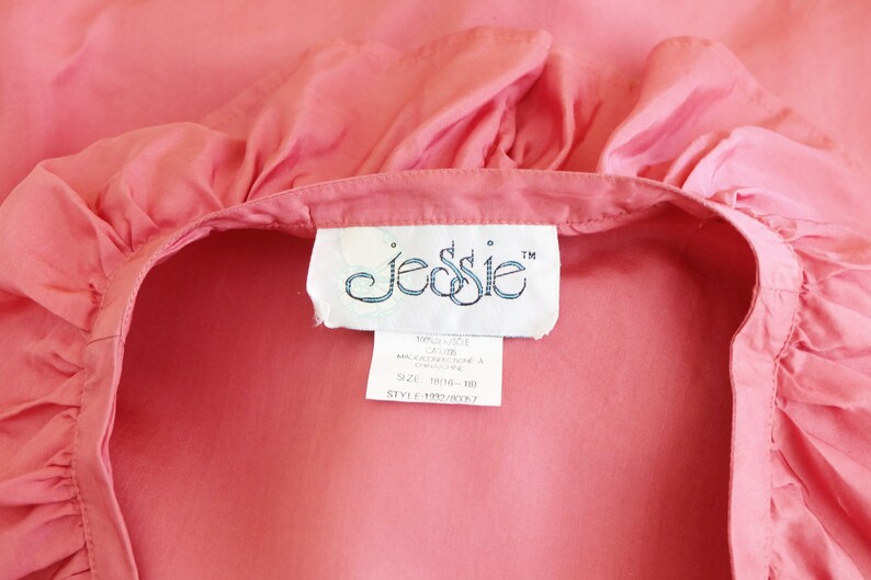 May include: A pink cotton blouse with a ruffled neckline and a white label that reads "JESSIE" with a trademark symbol.