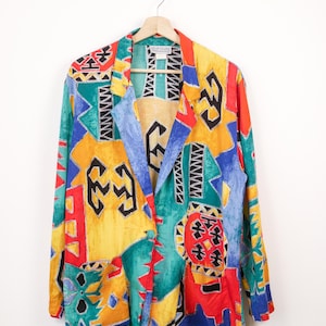 May include: A long-sleeve blazer featuring a vibrant, multi-coloured abstract geometric print in shades of yellow, red, blue, and green. The garment has a notched lapel, a single front button closure, and two large patch pockets. A Kelly Stevens label is visible.