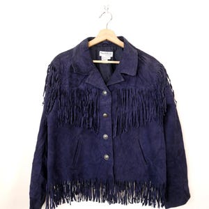 Può includere: Giacca in camoscio blu navy con frange sul petto, sulle maniche e sull'orlo. La giacca ha una chiusura con bottoni e un colletto. Il marchio "Nord Style" è visibile sull'etichetta.