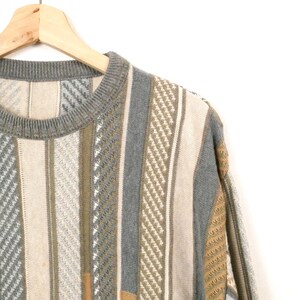 Puede incluir: Un su&eacute;ter vintage con rayas verticales en beige, gris y verde oliva. El su&eacute;ter est&aacute; colgado en una percha de madera sobre un fondo blanco. El patr&oacute;n de punto incluye varias texturas y dise&ntilde;os.