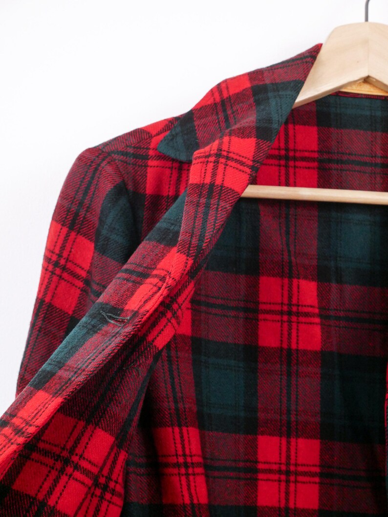 May include: A red and black plaid flannel shirt hanging on a wooden hanger. The shirt's pattern features a classic grid design with alternating red and black squares, and a touch of dark green. The collar and inner lining are visible.