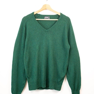 Peut inclure: Un pull à col en V et manches longues d'une couleur vert forêt foncé unie. Le vêtement présente une texture en tricot côtelé au niveau des poignets et de l'ourlet. Une petite étiquette rectangulaire avec le texte Puritan est cousue à l'intérieur.