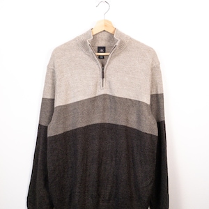 May include: A long-sleeve quarter-zip sweater featuring a color-blocked design in shades of light beige, medium gray, and dark charcoal. The knit garment has a ribbed mock neck collar, ribbed cuffs, and a ribbed hem with a central metal zipper pull.