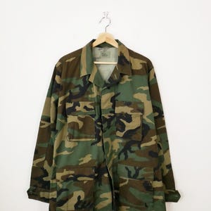May include: A green, brown and black camouflage jacket with a button-up front and two large pockets on the front.