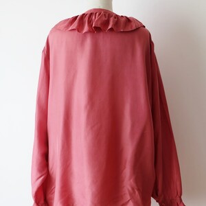 May include: A long-sleeved, salmon-colored blouse with a ruffled collar and cuffs. The blouse is made of a soft, silky fabric.