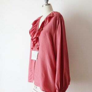 May include: A salmon-colored blouse with a large ruffled collar and long sleeves. The blouse has a button closure and a tag that says "Silk 100%".