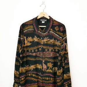 May include: Black button-down shirt with a safari-themed pattern. The shirt features giraffe, elephant, and leaf designs in shades of brown, gold, and burgundy. The shirt is hanging on a wooden hanger against a white background.