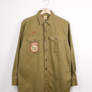 May include: A white ceramic mug with a black handle and the text "But First, Coffee" in a handwritten style. The mug is on a white surface. The mug is approximately 10 cm tall.