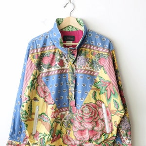 Könnte beinhalten: Ein blaues, gelbes, rosa und grünes, gemustertes Hemd mit Knöpfen, Kragen und langen Ärmeln. Das Hemd hat einen Reißverschluss auf der linken Seite und ein Etikett mit der Aufschrift "Jantzen" am Kragen.