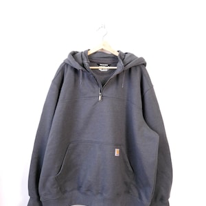 May include: A charcoal gray hooded sweatshirt with a half-zip closure and a front kangaroo pocket. The sweatshirt features a small, rectangular logo patch on the pocket and is hanging on a wooden hanger.