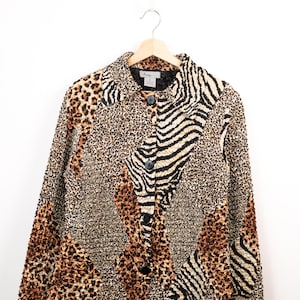 May include: A long-sleeved button-down jacket featuring a textured, crinkled fabric with a patchwork design of leopard and zebra animal prints in shades of brown, black, and tan. The garment includes a standard collar and four black circular buttons.