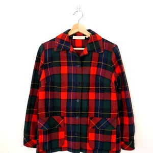 May include: A long-sleeved button-down jacket featuring a vibrant plaid pattern in shades of bright red, forest green, and navy blue. The jacket includes a pointed collar, five dark buttons down the front, and two square patch pockets at the waist.