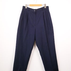 May include: Navy blue pleated trousers hanging on a wooden hanger. The pants have a button closure and a classic, tailored design. The fabric appears to be a medium-weight material.