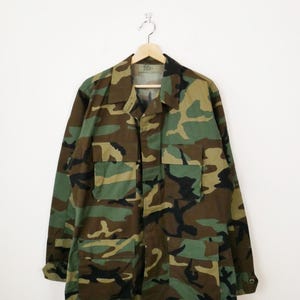 May include: A green, brown and black camouflage jacket with a button-up front and multiple pockets.