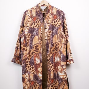 May include: A long, open-front jacket with a patchwork design featuring animal print and geometric patterns in shades of brown, tan, and burgundy. The jacket has a mandarin collar and is hanging on a wooden hanger.