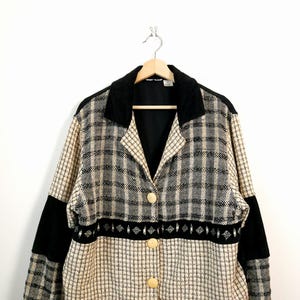 May include: A vintage blazer with a black velvet collar and accents. The jacket features a beige and black plaid pattern with black panels on the sleeves. It has three large, round, beige buttons.