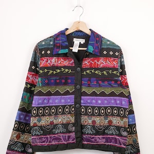 Puede incluir: Chaqueta acolchada colorida, con base negra y paneles estampados variados. La chaqueta tiene cierre de botones y cuello. Los paneles presentan diseños florales, geométricos y abstractos en tonos rojos, morados, azules y verdes.