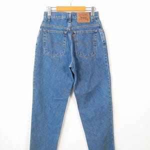 Może przedstawiać: Dżinsy z niebieskiego denimu z brązową sk&oacute;rzaną naszywką na tylnej kieszeni, na kt&oacute;rej widnieje napis "Levi's" białymi literami.