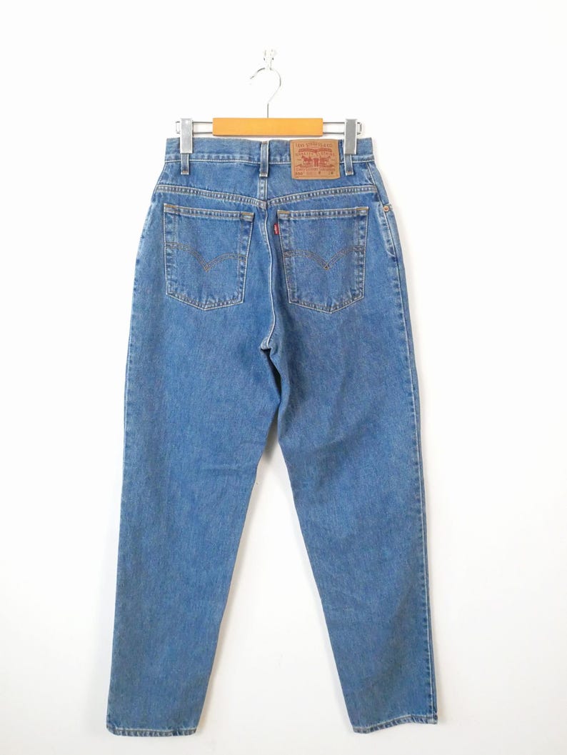 Może przedstawiać: Dżinsy z niebieskiego denimu z brązową sk&oacute;rzaną naszywką na tylnej kieszeni, na kt&oacute;rej widnieje napis "Levi's" białymi literami.
