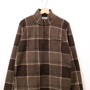 May include: A brown and dark brown plaid fleece pullover featuring a quarter-zip mock neck collar, long sleeves, and a small horizontal zippered pocket on the upper left chest. The garment has a soft texture and a repeating grid pattern.