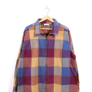 May include: A patchwork jacket in a checkerboard pattern of blue, purple, tan, and grey squares, with a full zip and a blue collar and cuffs. The jacket is suspended on a wooden hanger.