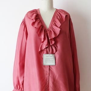 May include: A salmon pink silk blouse with a large ruffled collar and long sleeves. The blouse has a button-up front and a tag that reads "100% Silk".