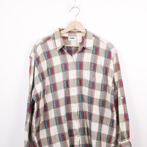May include: A long-sleeved shirt with a plaid design in white, grey, and brown. The shirt has colourful arrow-shaped patterns in red, teal, and purple. The brand name "GITANO" is visible on the label.