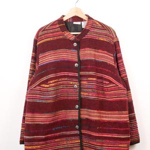 May include: A burgundy jacket with horizontal stripes in various colors, including red, yellow, and blue. The jacket has a round collar, long sleeves, and three decorative buttons. Black trim outlines the collar and front.