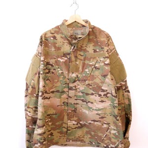 May include: A long-sleeved jacket featuring a multi-coloured camouflage pattern in shades of tan, brown, green, and black. The jacket includes a high collar, a front zip closure, and rectangular hook-and-loop patches on the chest and sleeves.
