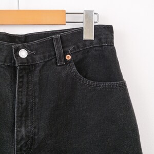 Op de afbeelding: Een zwarte spijkerbroek van denim met een hoge taille, een zilverkleurige metalen knoopsluiting, een klassieke vijf-pocket constructie met verstevigde klinknagels en zichtbare stiksels langs de tailleband en de randen van de zakken.
