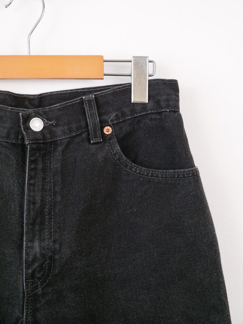Op de afbeelding: Een zwarte spijkerbroek van denim met een hoge taille, een zilverkleurige metalen knoopsluiting, een klassieke vijf-pocket constructie met verstevigde klinknagels en zichtbare stiksels langs de tailleband en de randen van de zakken.