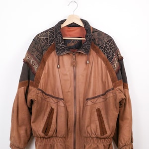 May include: A vintage brown leather jacket with a zip-up front, featuring geometric patterns on the shoulders and collar. The jacket has two front pockets and a ribbed hem. The brand name "Winlit" is visible on the collar.