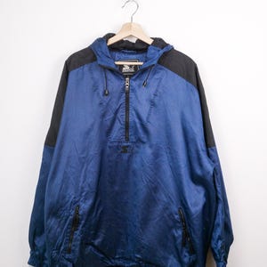 May include: Blue and black Starter anorak jacket with a hood and a half-zip closure. The jacket has a Starter logo on the chest and a drawstring at the hem. Features two zippered pockets and black shoulder panels.
