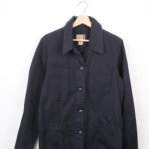 May include: A dark navy blue jacket with a collared neckline, four front pockets, and button closures. The jacket is hanging on a wooden hanger against a white background. The brand name "ATI" is visible on the label.