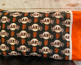 May include: A black pillowcase with a repeating pattern of orange baseballs and the words "SF Giants". The pillowcase has a white border and an orange edge.
