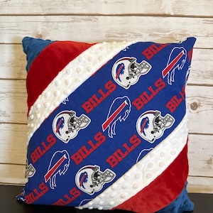 May include: Square pillow with a blue, red, and white design. The pillow features a blue section with the word "BILLS" and Buffalo Bills helmet and logo graphics. The pillow has a red and white striped pattern and a blue backing.
