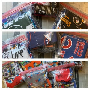 May include: Multiple clear plastic bags filled with various colorful fabric scraps. The fabrics feature sports team logos, including the Jets, Steelers, Cubs, and a variety of other patterns.