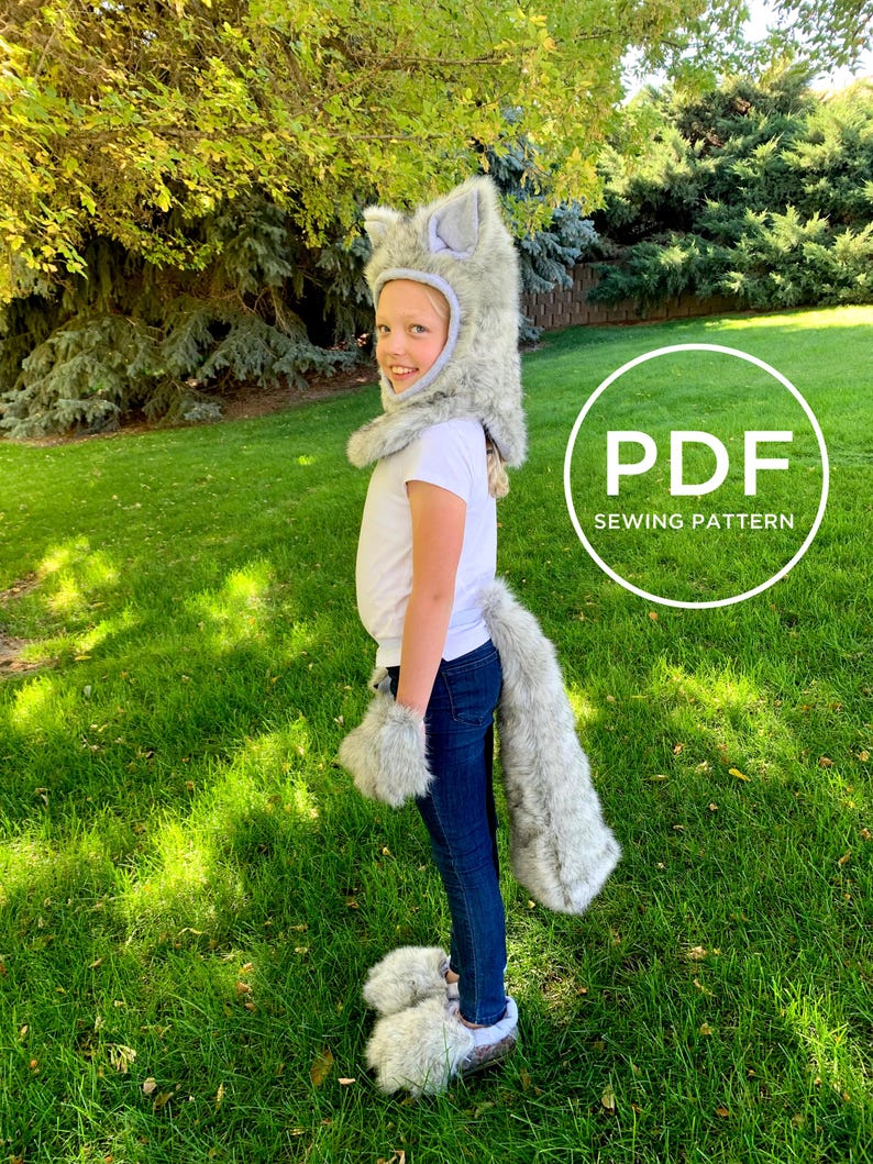 May include: A child wearing a grey wolf costume with a hood, tail and paw mitts. The costume is made of soft, fluffy fabric. The child is standing on a grassy lawn. The image includes the text "PDF SEWING PATTERN".