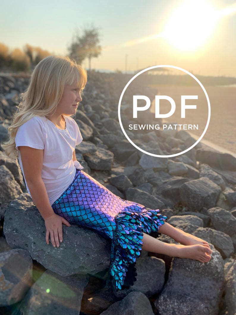 May include: A girl wearing a white shirt and a mermaid tail skirt with iridescent blue and purple scales. The skirt has a ruffle at the bottom. The girl is sitting on rocks by the water. The image has a circle with the text "PDF SEWING PATTERN" in white.