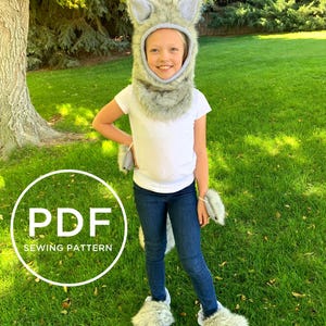 May include: A PDF sewing pattern for a wolf costume. The pattern includes a hooded headpiece, paw mitts, and foot coverings. The costume is made of grey faux fur and is shown being worn by a child.