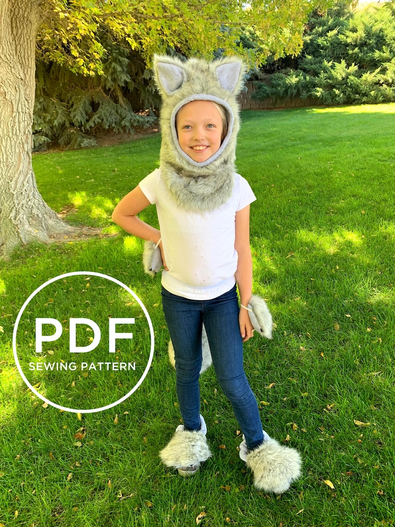 May include: A PDF sewing pattern for a wolf costume. The pattern includes a hooded headpiece, paw mitts, and foot coverings. The costume is made of grey faux fur and is shown being worn by a child.