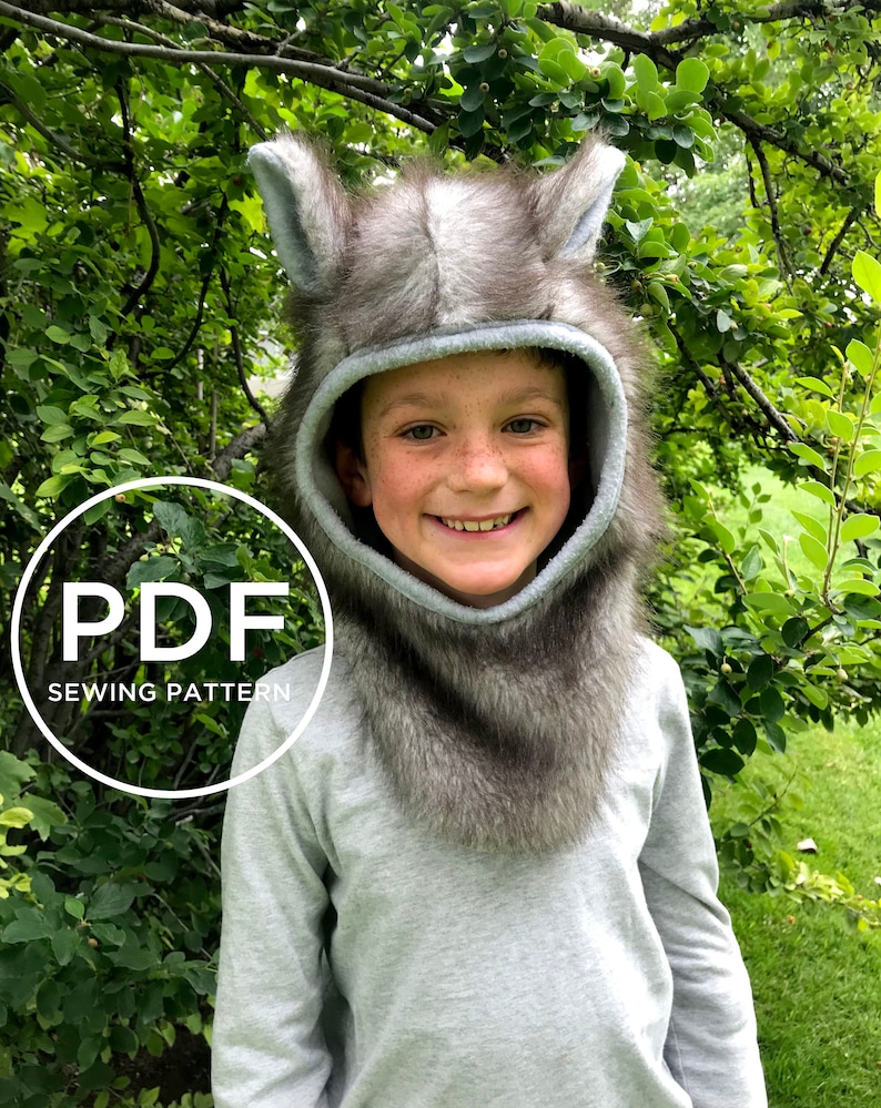 May include: A PDF sewing pattern for a wolf hooded hat. The hat is made of grey faux fur and has a light blue lining. The pattern is for a child's size.