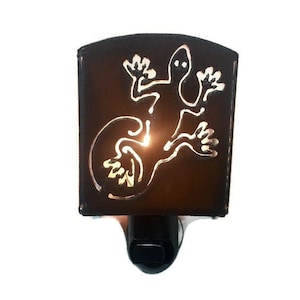 May include: A brown metal night light shaped like a lizard with a white outline. The light is on and glowing.