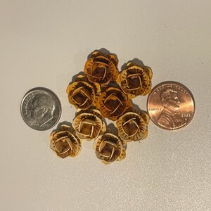 May include: A group of eight small, decorative, gold-colored buttons with a floral design. The buttons are about the size of a US penny.