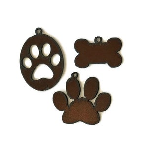 May include: Three brown metal pet-themed charms. One is a paw print inside a circle, another is a bone shape, and the third is a paw print. Each charm has a small hole for hanging.