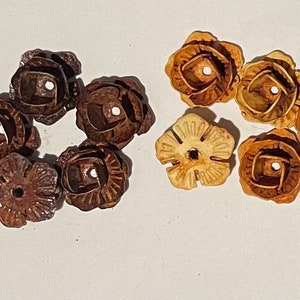 May include: Two sets of six decorative flower-shaped metal embellishments. One set is brown and the other is light brown.